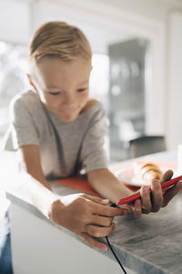 Boy charging smart phone at dining table in room