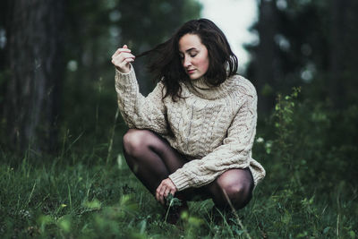 Young woman sitting on grass against trees