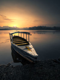 Boat moored on lake against sky during sunset