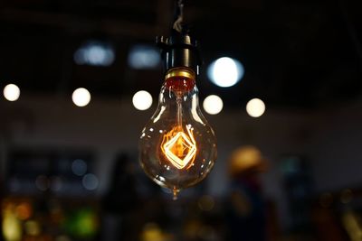 Close-up of illuminated light bulb hanging in room