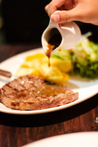 Cropped image of hand pouring gravy on meat in plate