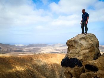 Man standing on rock by mountain against sky