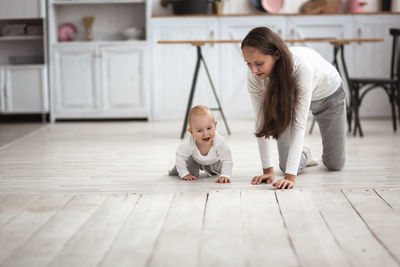 Beautiful mother with long hair and baby crawling together on the floor, lifestyle .