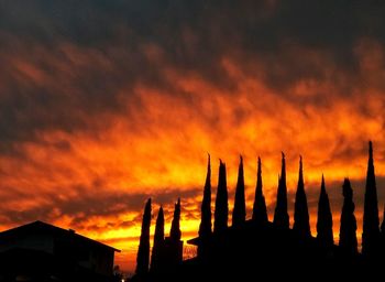 Silhouette cranes against dramatic sky during sunset