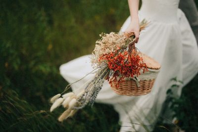 Close-up of bride holding flowering plants with basket