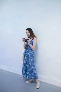 Full length of woman holding camera standing against wall