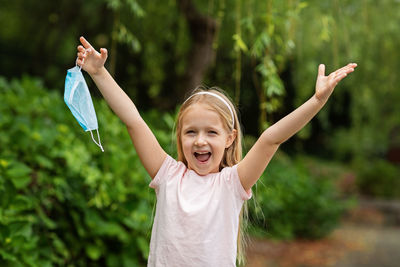 Portrait of happy girl with arms raised holding mask