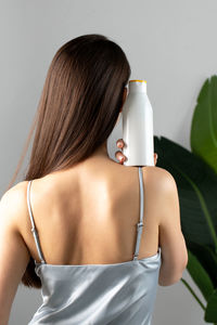 Woman holds a white bottle of cosmetics in her hand, standing with her back to the camera. 