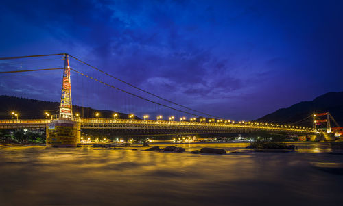 Illuminated bridge over river against sky at night