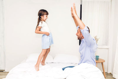 Father playing with daughter on bed at home