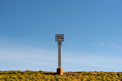 Low angle view of river milestone against clear blue sky