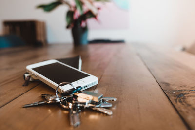 Close-up of mobile phone with keys on wooden table at home