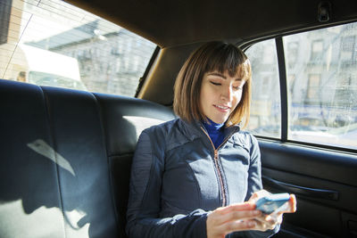 Woman using smart phone while traveling in taxi