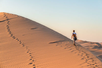 Rear view of woman walking on desert against sky