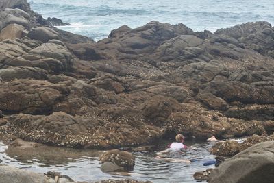 Rear view of woman sitting on rock by sea