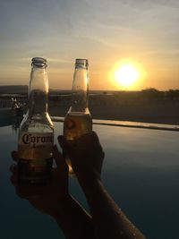 Close-up of hand holding bottle against sky during sunset