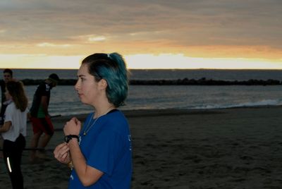 Young woman standing on beach against sky during sunset