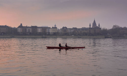 Man rowing boat on river against sky during sunset