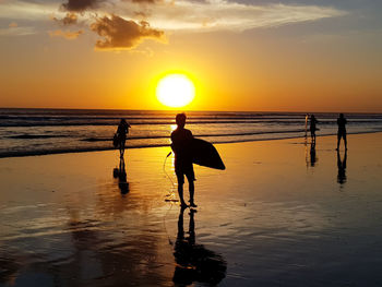 Silhouette people on beach against sky during sunset
