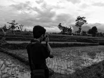 Male photographer photographing through camera while standing on field