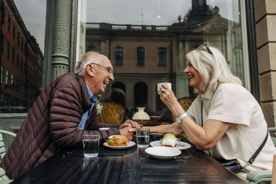 Happy senior man holding hand of woman while sitting together at sidewalk cafe