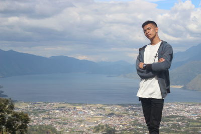 Portrait of teenage boy with arms crossed while standing against mountains 