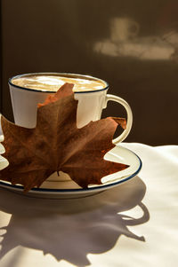 Close-up of morning coffee cup on table and the sun is shinning on coffee. there is a yellow leaf.