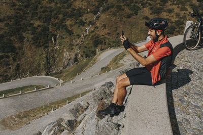 Cyclist photographing through smart phone sitting on wall at gotthard pass