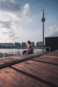 Side view of woman with umbrella against sky in city