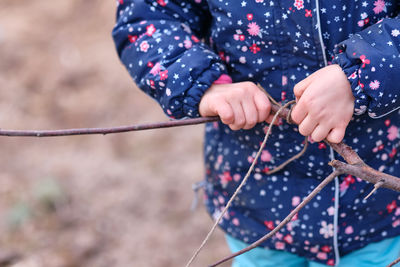 Midsection of girl tying rope to stick while standing outdoors