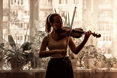 Silhouette of a young girl, a musician. playing the violin in the background of the window.