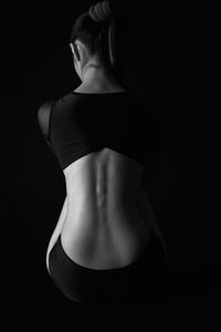 Rear view of woman in body suit standing against black background