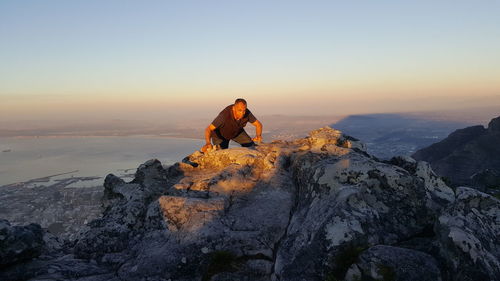 Man climbing mountain against sky during sunset