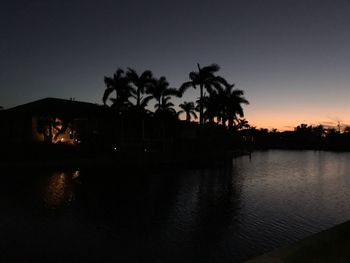 Silhouette palm trees by lake against sky at night