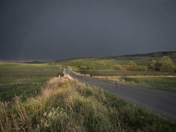 Empty road amidst field against sky