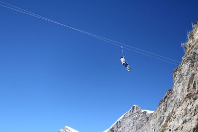 Low angle view of person hanging on zip line against clear sky