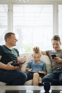 Smiling fathers talking while son using digital tablet at home