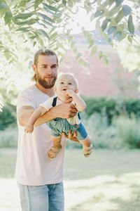 Smiling father holding sun while standing at park