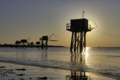 Silhouette cranes on beach against sky during sunset