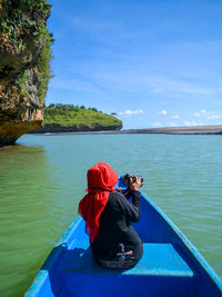 Rear view of woman photographing while sitting in boat on sea