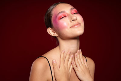 Young woman with closed eyes against maroon background