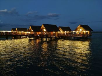 Illuminated building by sea against sky at night