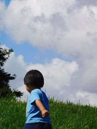 Rear view of boy walking on land against cloudy sky