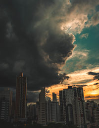 Buildings in city against dramatic sky during sunset