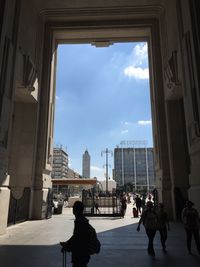 People walking in city against cloudy sky