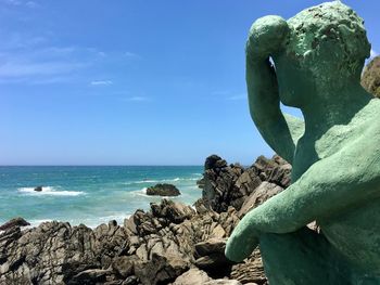 Statue on rock by sea against blue sky