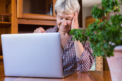 Tired senior mature caucasian woman suffering from headache while using laptop at home