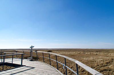 Boardwalk over field against clear blue sky