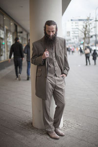 Thoughtful bearded mature man standing by column on footpath