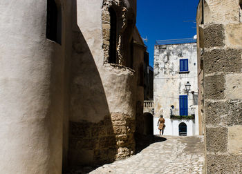 Rear view of woman walking amidst old buildings on sunny day